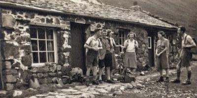 Black and white archive photo of a group of travellers outside a stone hostel building