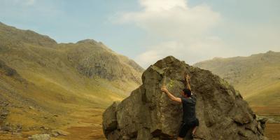 Man climbing a large boulder surrounded by moutains