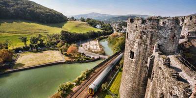 Train travelling past a castle with countryside on the other side of the track