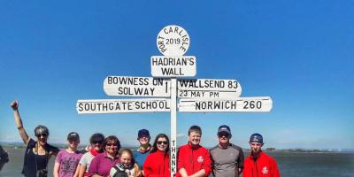 Group of adults and children posting next to a sign for Hadrian's Wall