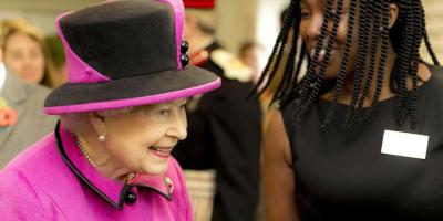 The Queen wearing a pink suit and hat while talking to a member of staff