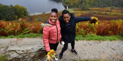 Two girls holding autumn leaves while standing by a lake