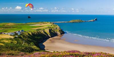 Glider sailing over a beach with blue sea and green cliffs