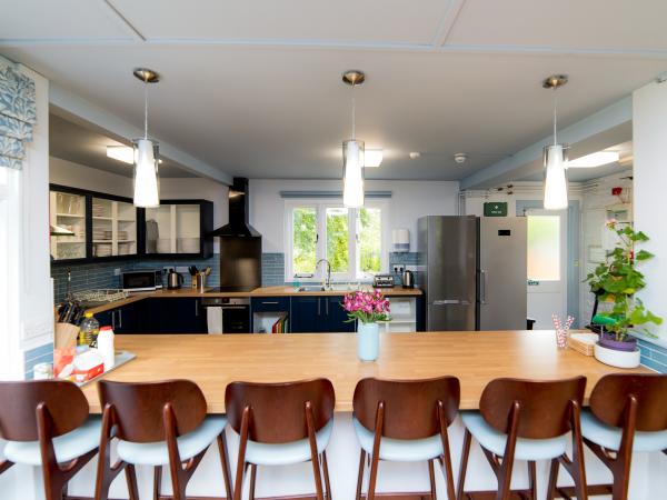 Open plan kitchen containing three hanging lights and a breakfast bar with six chairs