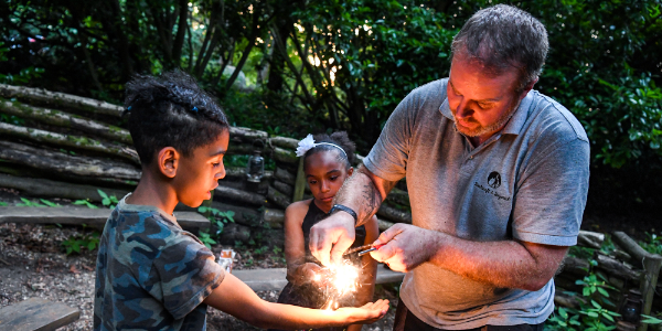 Leader showing child how to light a campfire